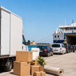 Delivery truck unloading cardboard boxes at a harbor with a large passenger ship docked in the background.